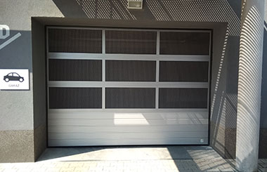 Moderní sekční garážová vrata s hliníkovými panely a skleněnými prvky pro komerční garáž, dostupná u společnosti VRATA-L&V, specializované na garážová řešení.